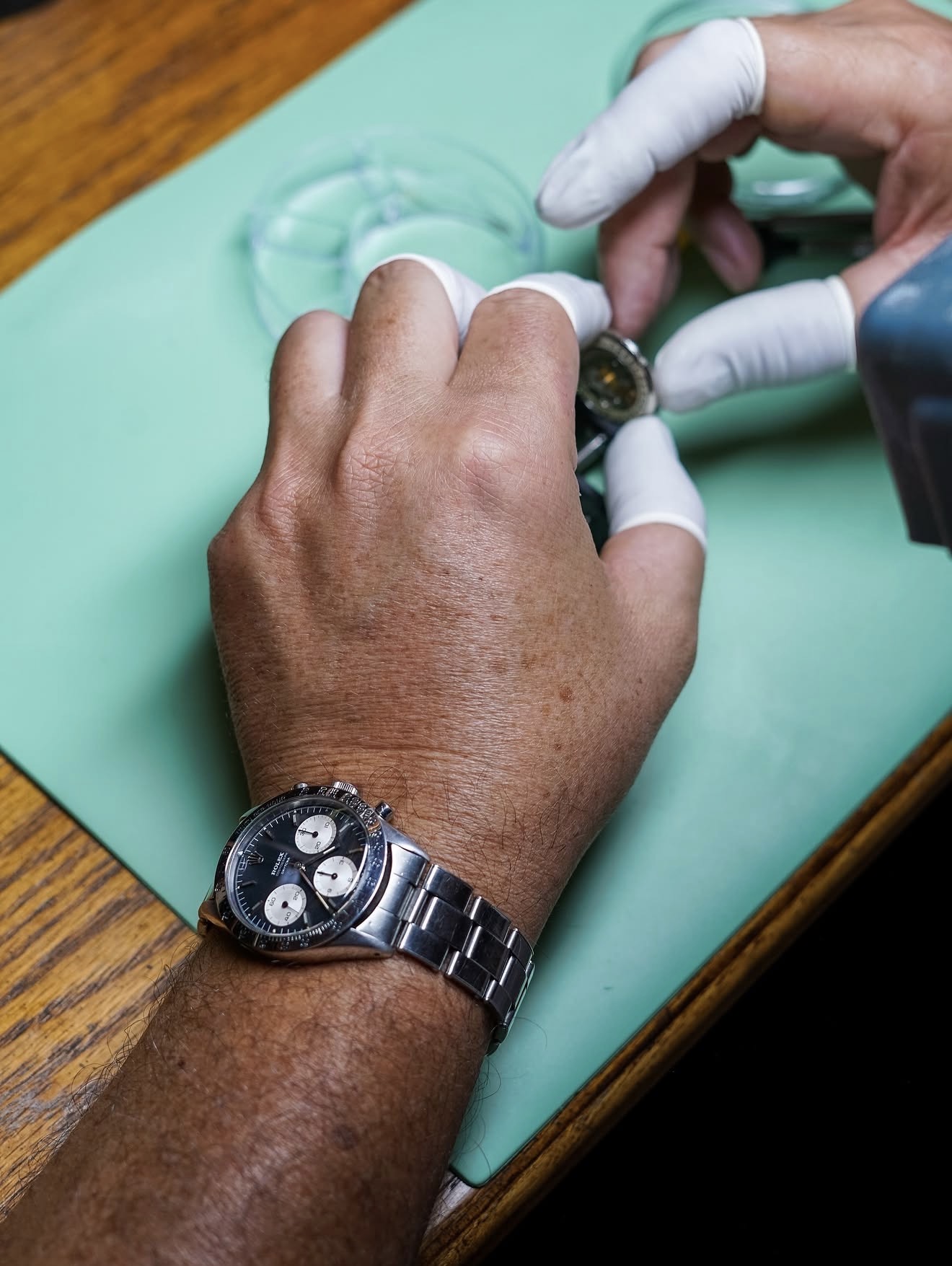 Vintage Rolex chronograph on wrist while a watchmaker services another piece