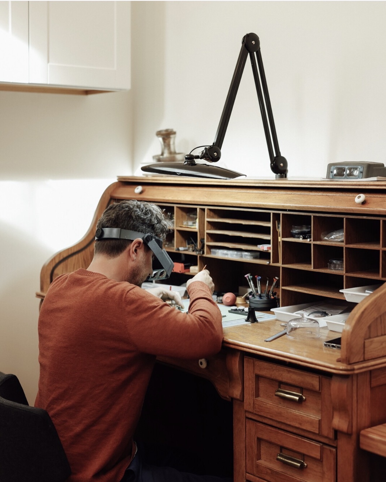 Watchmaker servicing a movement at a vintage roll-top workbench
