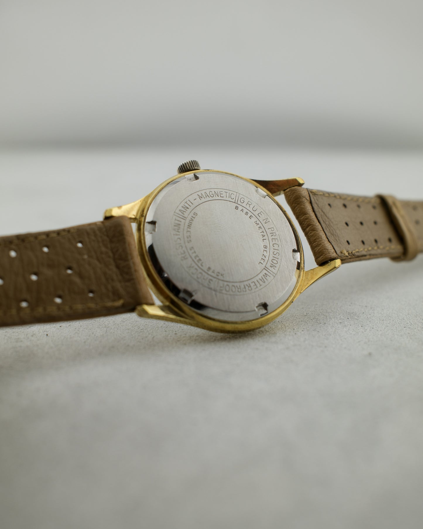 1960's vintage Gruen watch with gold plated case and a stainless steel screw down case back stating "anti magnetic", "shock resistant", and "waterproof". Wearing a light brown strap.