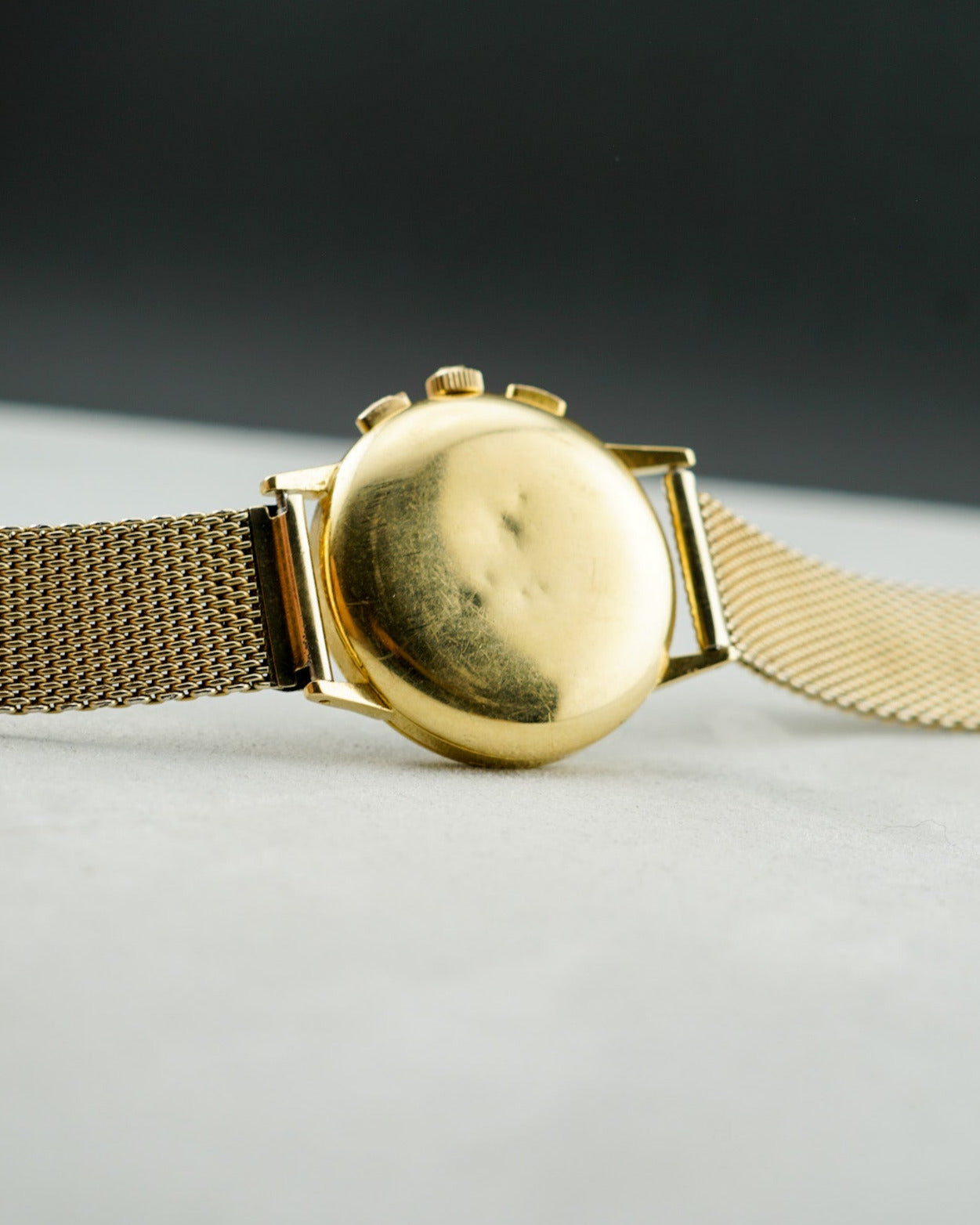 Gold wristwatch on a light gray surface with a dark background