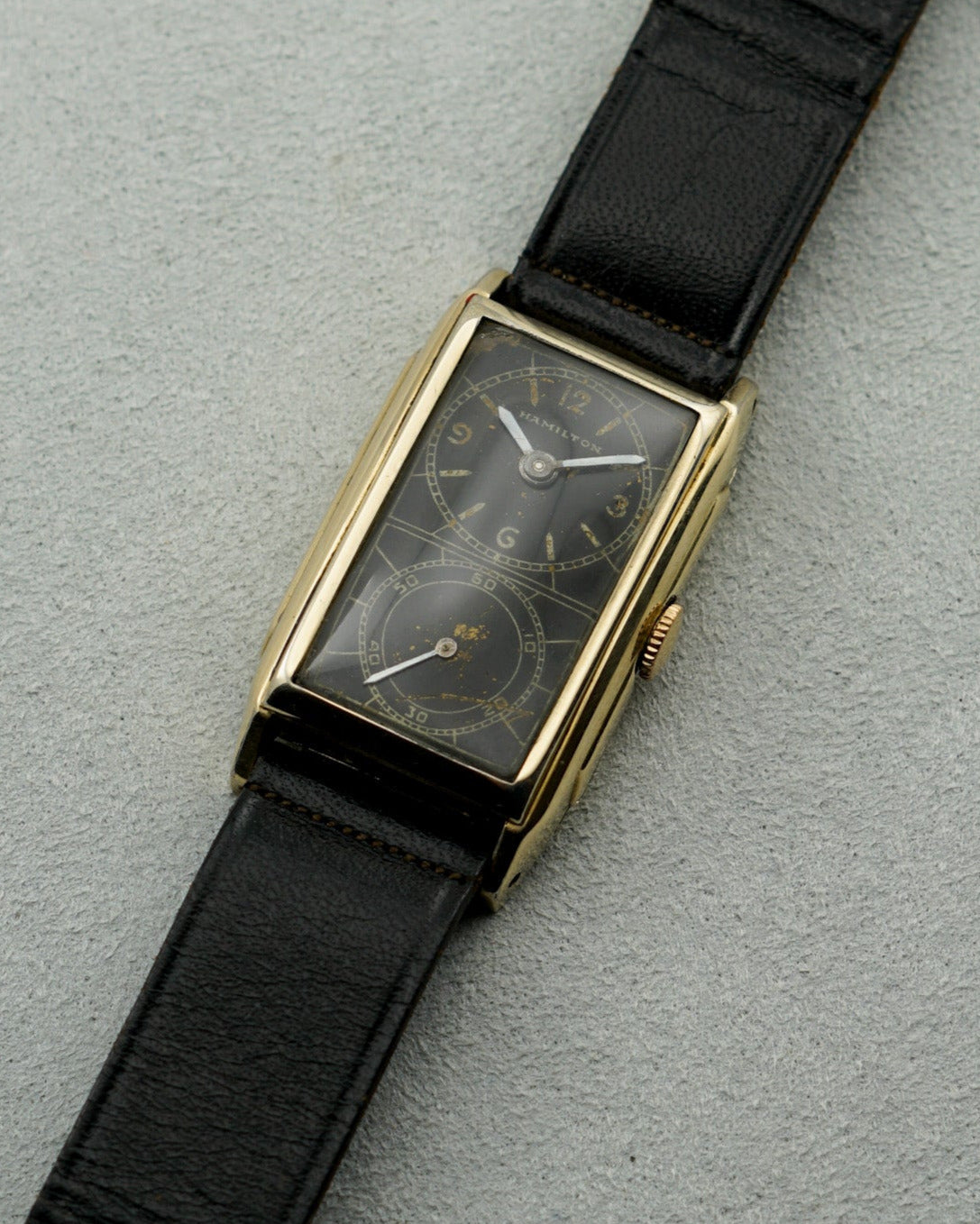 Vintage watch with black strap and gold case on a gray background