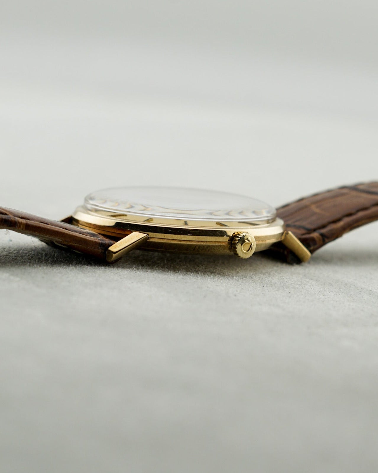 Watch with brown leather strap and gold case on a light gray background