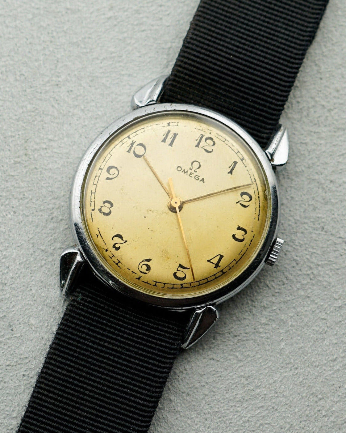 Vintage watch with black strap and gold face on a gray background