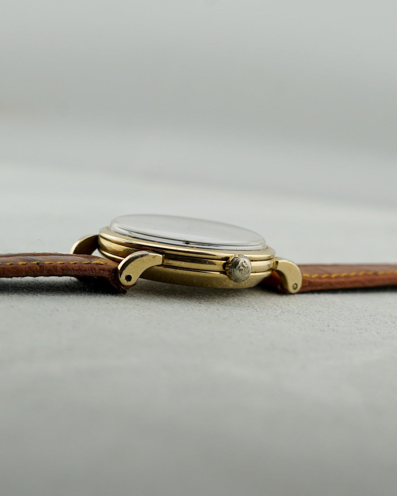 Gold watch with brown leather strap on a light gray background
