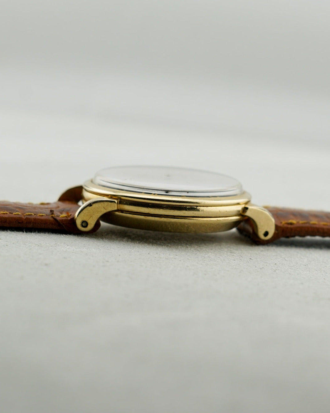 Gold watch with a brown leather strap on a light gray background