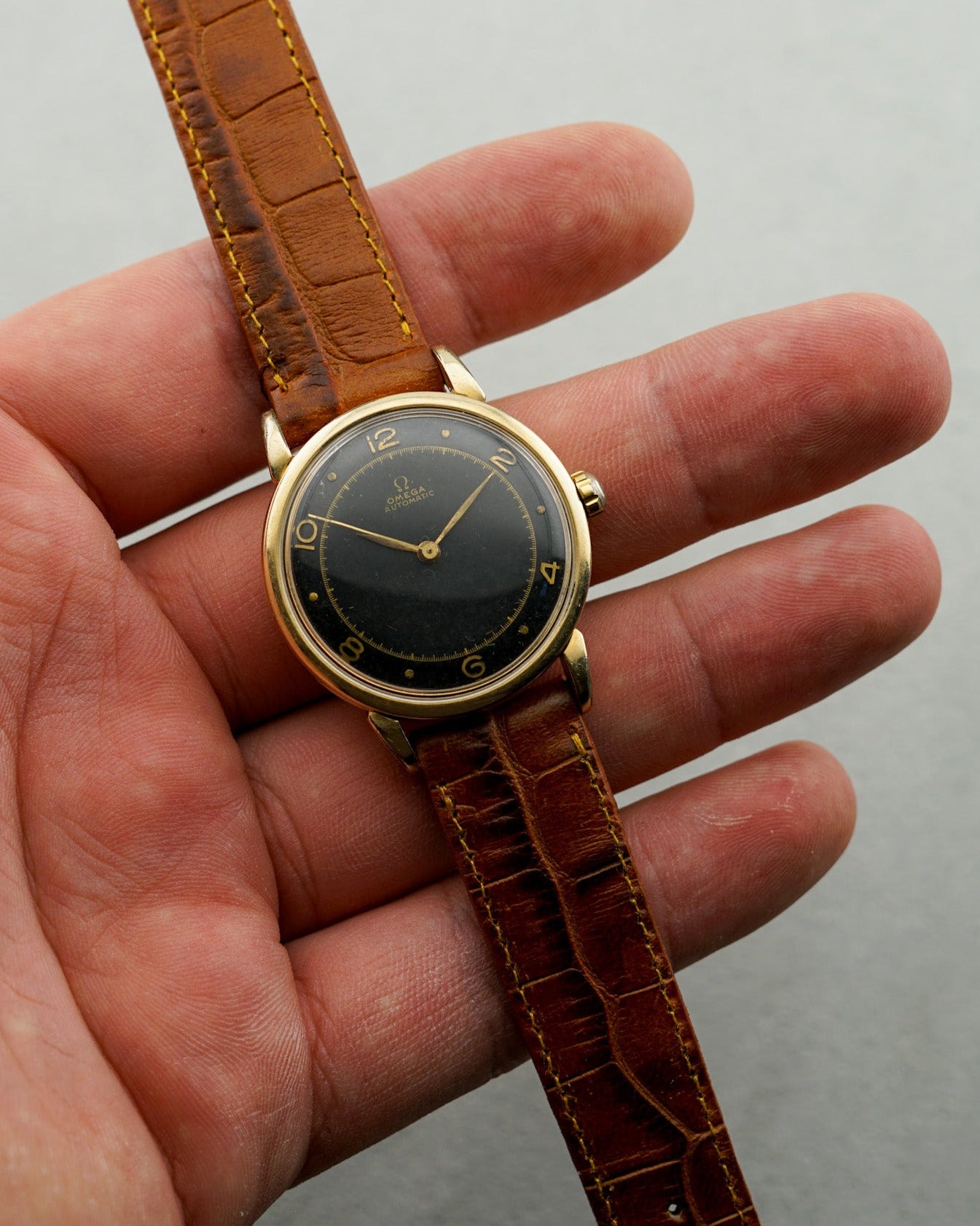 Vintage watch with brown leather strap held in a hand against a neutral background