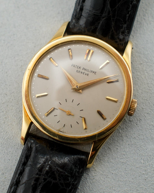 Vintage 1960's Patek Philippe watch with 18 karat yellow gold case, white dial, gold hands and small seconds hand, and black leather strap.